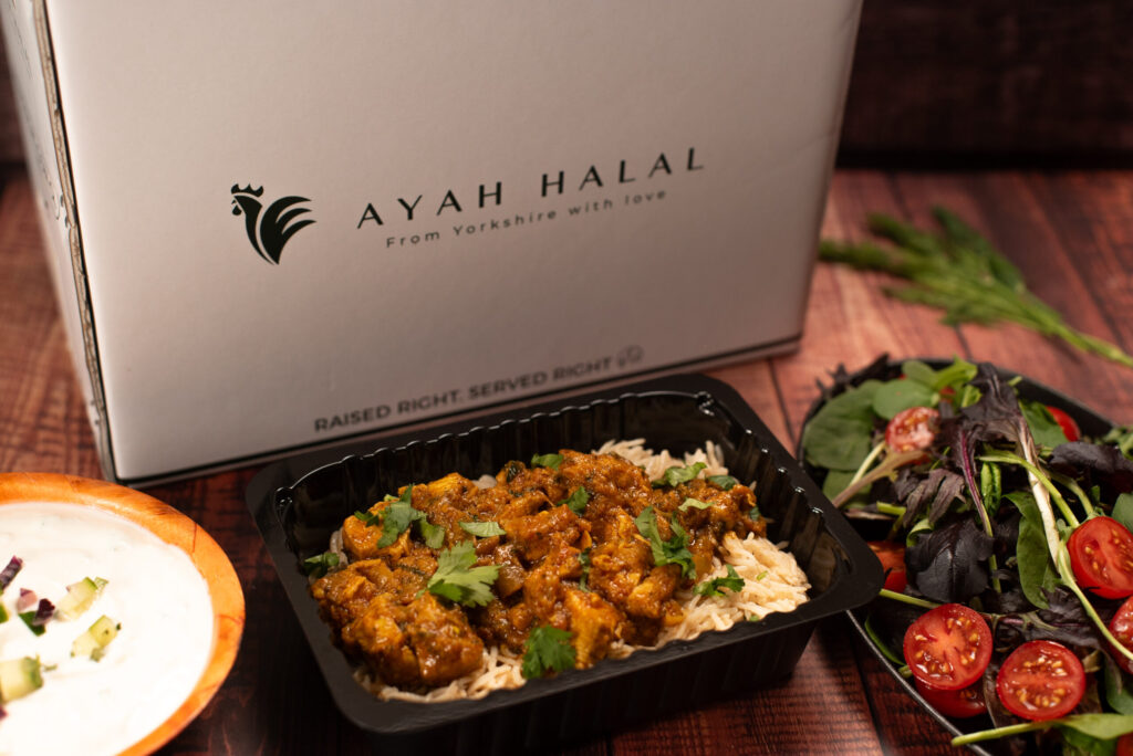 Halal meal delivery with chicken curry and basmati rice, fresh salad, yogurt raita, and AYAH HALAL branded packaging on rustic wooden table.