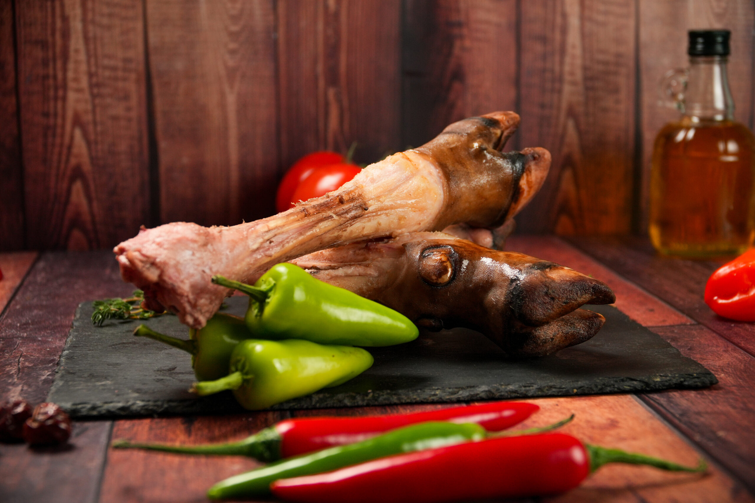 Raw halal lamb trotters (paya) on a slate board, cleaned sheep feet with visible bone and skin, served with chillies and herbs on a rustic wooden background