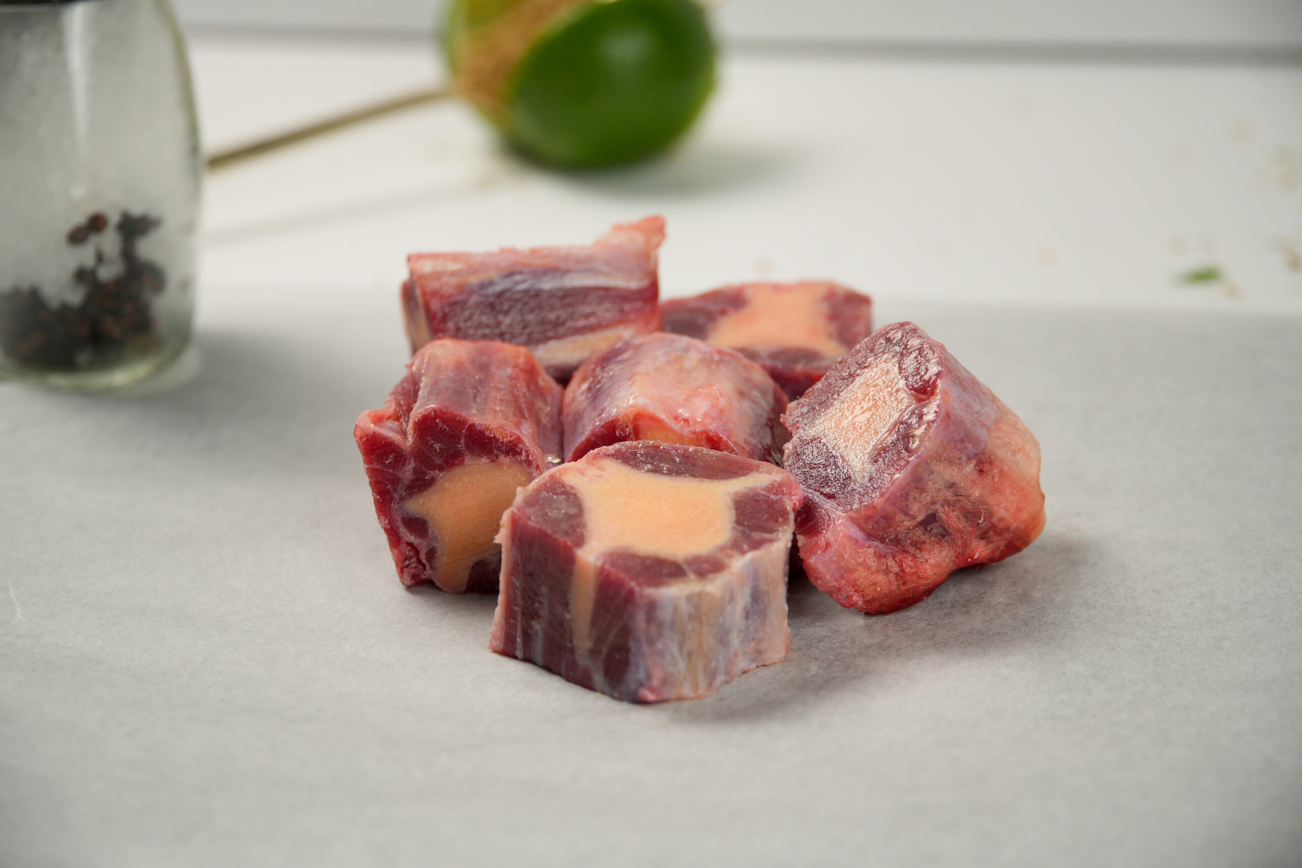 Raw halal oxtail cuts with bone marrow pieces on parchment paper, fresh butcher meat portions with visible bone centre, clean food prep setting