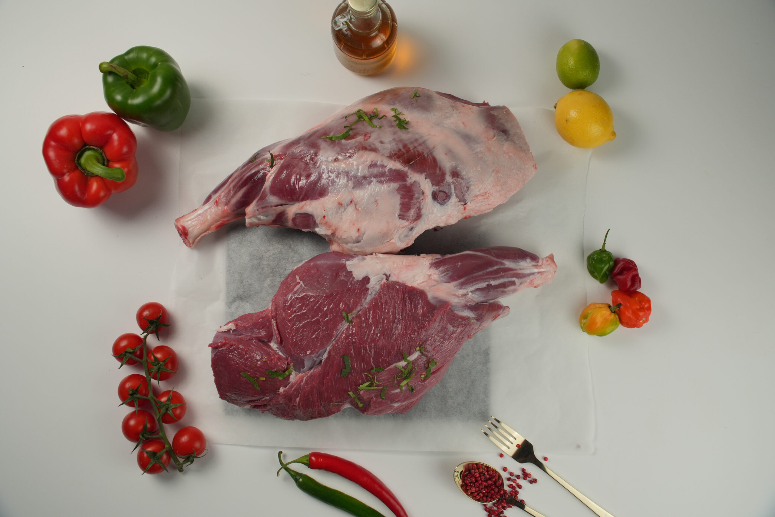 Raw halal lamb leg cuts on parchment paper, fresh bone-in meat with herbs, surrounded by vegetables, spices, and cooking ingredients on a clean surface