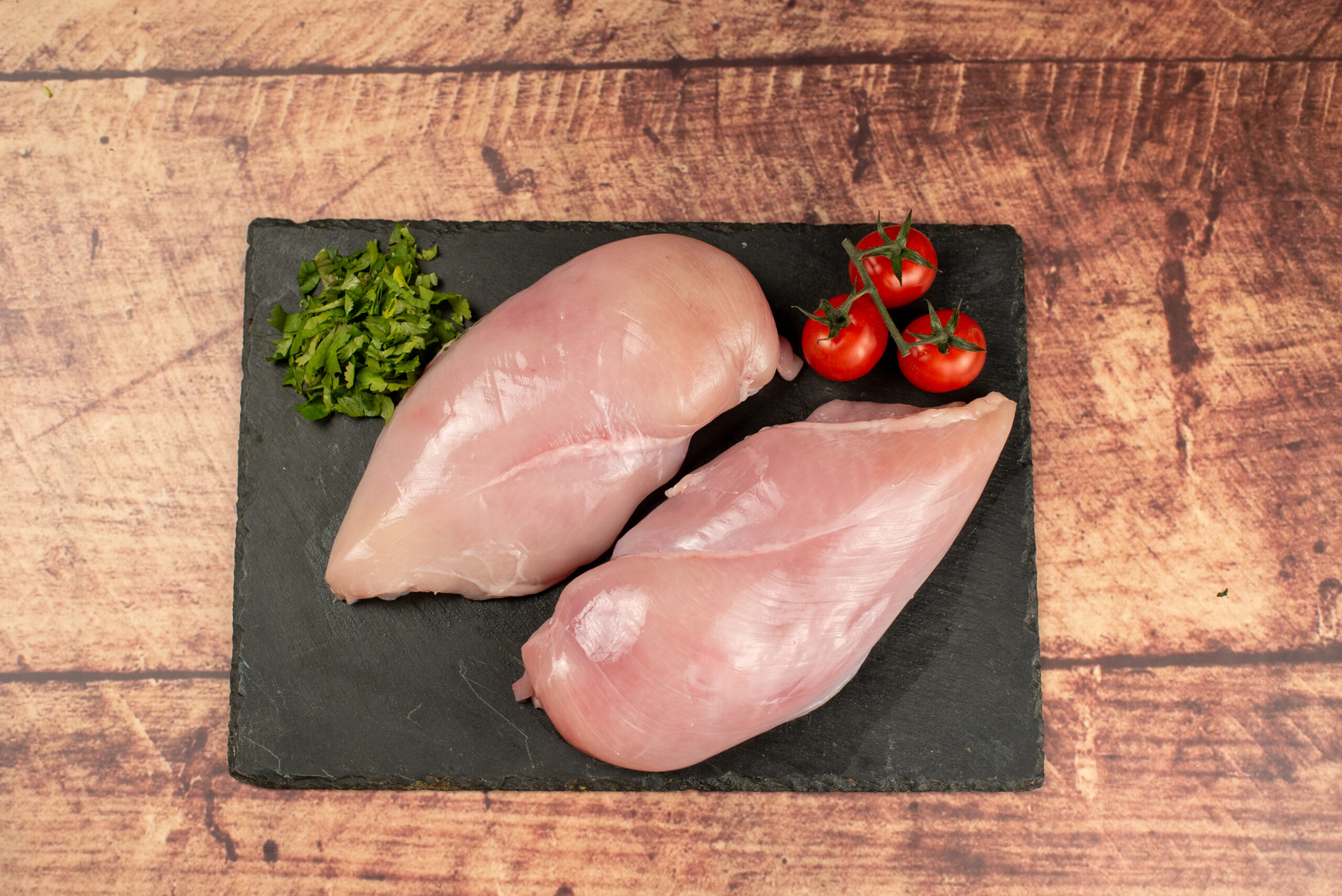 Fresh halal chicken breast fillets on slate board with parsley and vine tomatoes