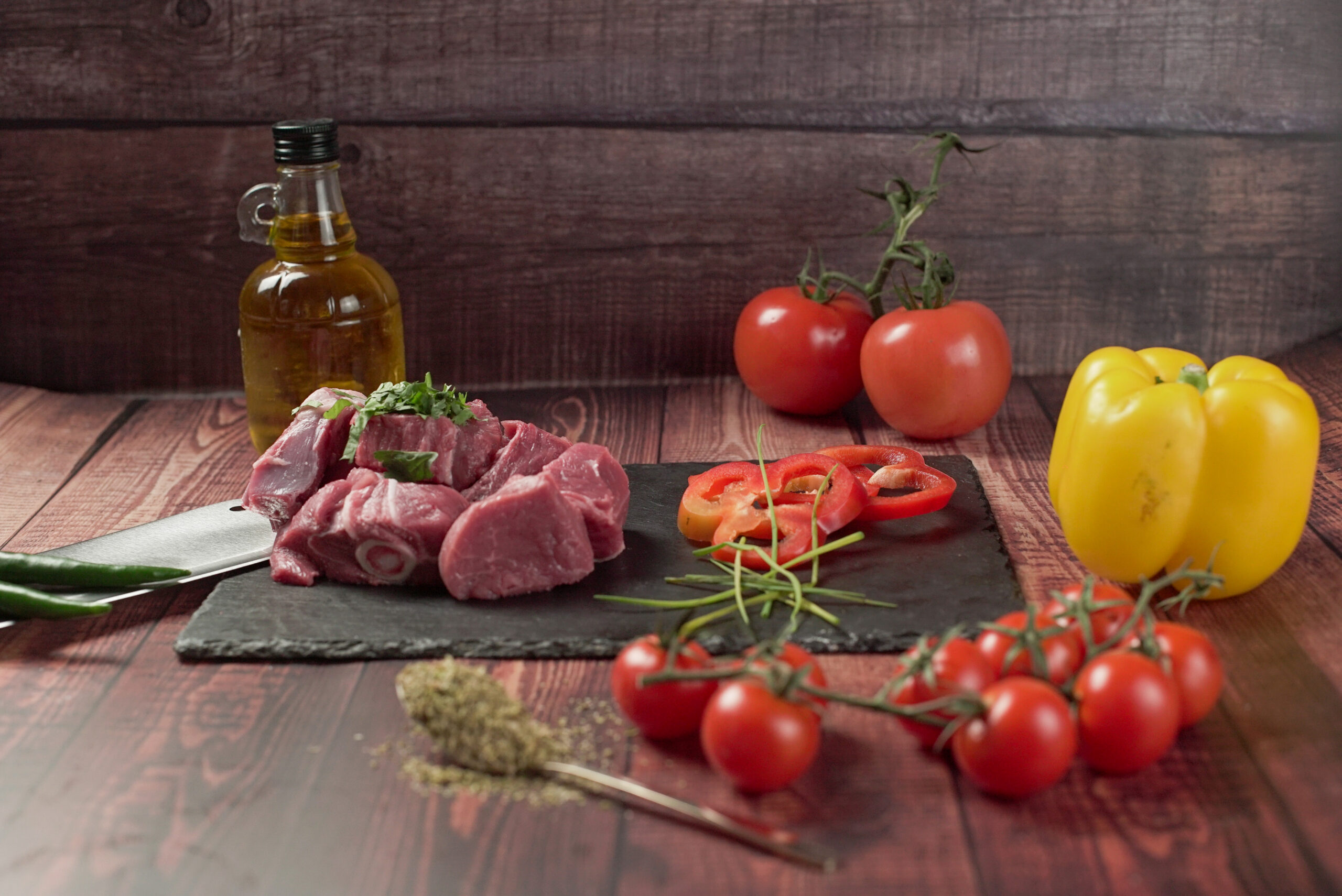 Raw halal lamb chunks prepared on slate board with peppers, tomatoes and oil