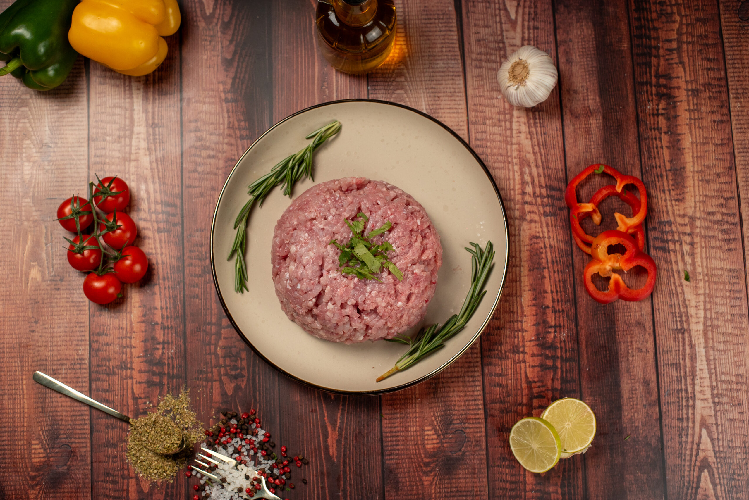 A plate of seasoned chicken mince surrounded by spices, resting on a rustic wooden table.
