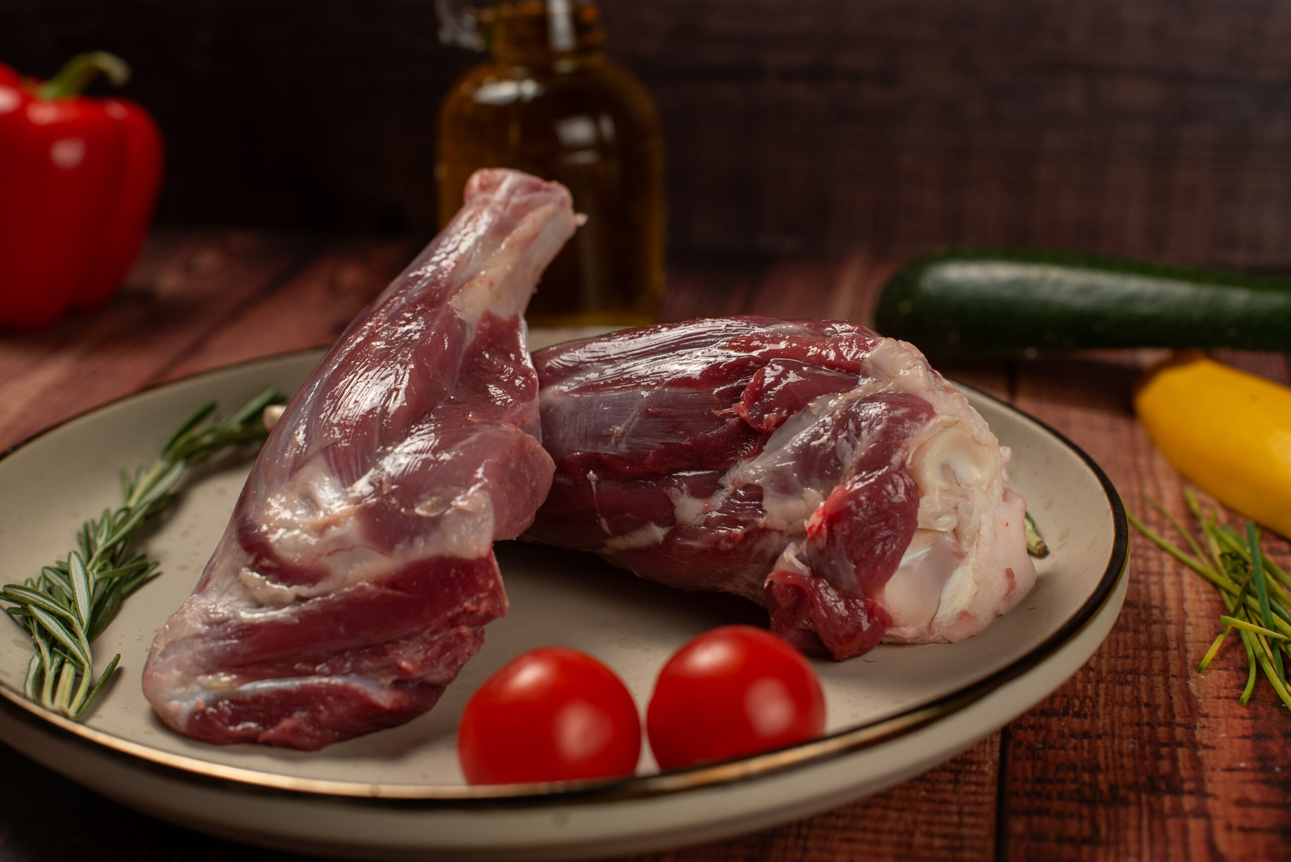 Close up of raw halal lamb shanks on plate with herbs